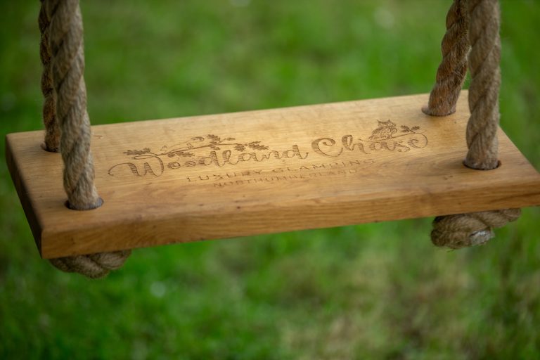 Close up image of Hospitality Photography wooden swing with name Woodland Chase Glamping