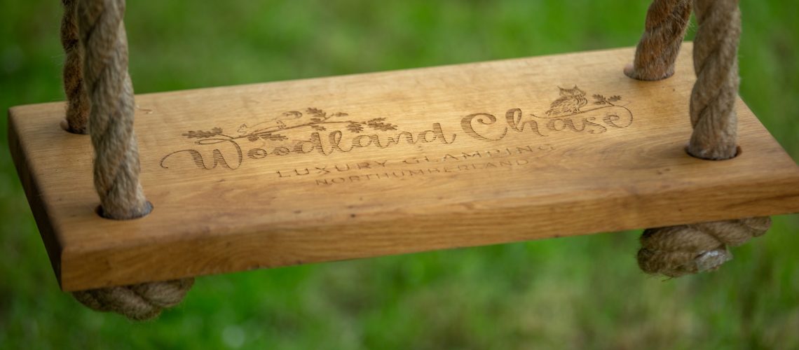 Close up image of Hospitality Photography wooden swing with name Woodland Chase Glamping